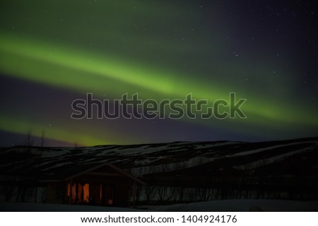 Northern lights with hut, trees and snowy mountains in iceland