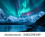 Northern lights over the snowy mountains, frozen sea, reflection in water at winter night in Lofoten, Norway. Aurora borealis and snowy rocks. Landscape with polar lights, road, starry sky and fjord