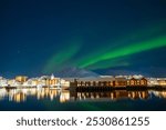 Northern lights over Svolvaer town on Lofoten islands, Norway. Winter night with Aurora borealis, reflection in water, snowy mountains and starry sky. Landscape with polar lights.