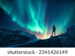 Northern lights and woman on mountain peak at night. Aurora borealis and silhouette of alone girl on mountain trail. Landscape with polar lights. Sky with stars and bright aurora. Travel background