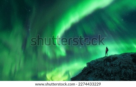 Northern lights and young woman on mountain peak at night. Aurora borealis and silhouette of alone girl on top of rock. Landscape with polar lights. Starry sky with bright aurora. Travel background