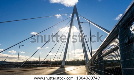 Northern Spire Bridge (opened Summer 2018) in Sunderland spanning the River Wear.  Photo taken facing the sun giving the bridge a silhouette contrasting with the blue sky with dark and white clouds.
