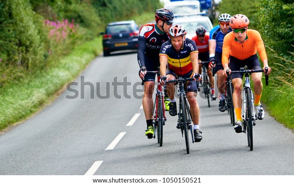 NORTHUMBERLAND, ENGLAND, UK - AUGUST 26, 2016: A\
group of cyclists on a bike race on a sunny day along busy country\
roads in the\
UK.