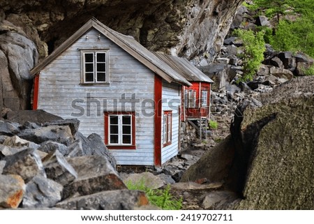 Norway landmark. Helleren old homes hidden beneath huge rock cliff overhang in Jossingfjord.