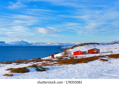 Norway in winter: mountains with red house and the ocean.