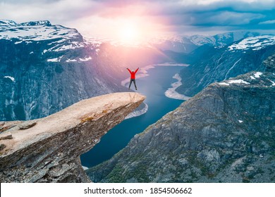 Norway, A woman Jump on the mountain's cliff edge of Trolltunga throning over Ringedalsvatnet  watching the sunset and snowy Norwegian mountains near Odda, Rogaland, Norway