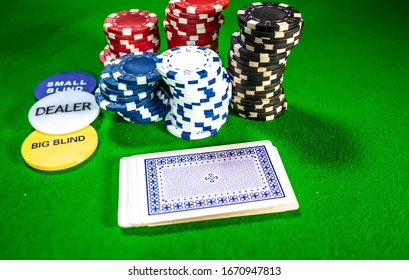 Norwich, Norfolk, UK – February 22 2020. Top Down View Of Dealer And Blind Buttons, Poker Chips And A Playing Cards Face Down On Green Baize