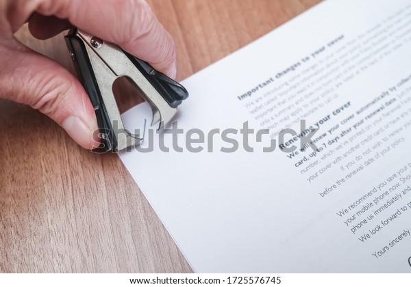 Norwich, Norfolk, UK - May 03 2020.\
Close up of human hand using a staple remover to remove a staple\
from sheets of paper on a wooden desk in a commercial\
office