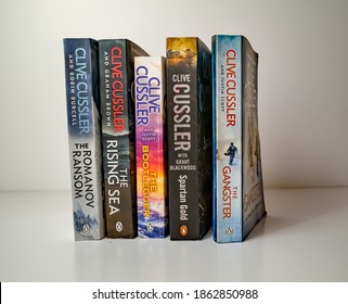 Norwich, Norfolk, UK – November 08 2020. Illustrative editorial photo of a selection of thriller genre paperback books written by Clive Cussler isolated against a white background.