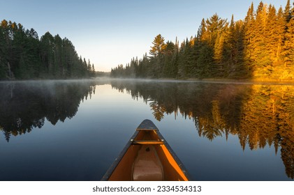 The nose of a yellow canoe sticking out in front on a glass calm late with steam and sun light hitting the tips of trees  - Powered by Shutterstock