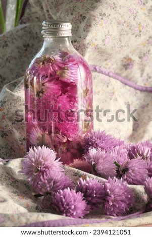 A nostalgic bottle is filled with vinegar made from chive flowers. In the foreground lush chive flowers.