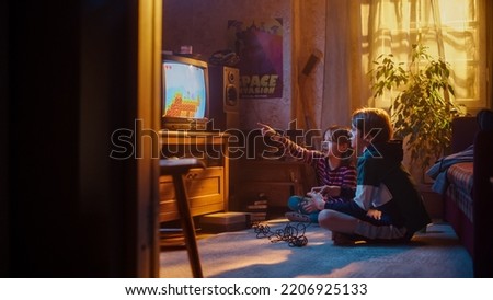Nostalgic Childhood Concept: Young Brother and Sister Playing Old-School Arcade Video Game on a Retro TV Set at Home in a Room with Period-Correct Interior. Friends Pass the Level and Win.