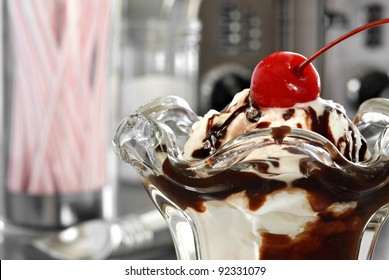 Nostalgic still life of hot fudge sundae in classic tulip dish with retro diner objects in background.  Macro with shallow dof.