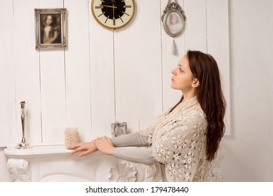 Nostalgic Young Woman In A Stylish Shawl Standing With Her Hands Resting On A Marble Mantelpiece Looking At An Old Family Portrait