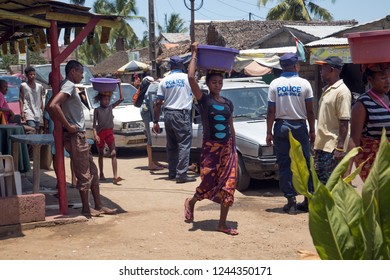 NOSY BE ISLAND, MADAGASCAR - OCTOBER 18,2018: Malagasy Women Walk Along A Busy Village Street With Basins On Their Heads