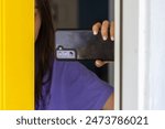 Nosy woman using phone camera to record neighborhood visitor from inside her front door.