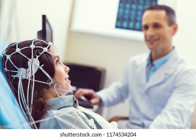 I am not afraid. Selective focus on a young lady smiling cheerfully while sitting in a lab and getting her brain analyzed during an electroencephalograph procedure.