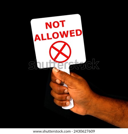 NOT ALLOWED sign board holding hand with black background close-up view, A hand holding sign board 