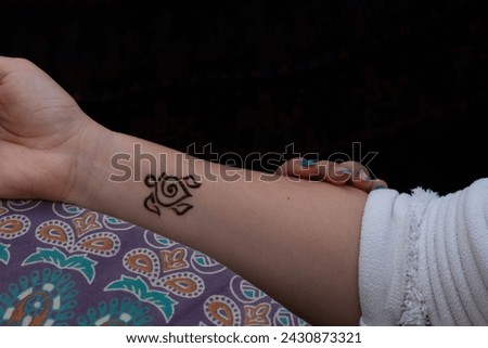 Not finished henna tattoo of an abstract turtle on a wrist with a colorful paisley dress background
