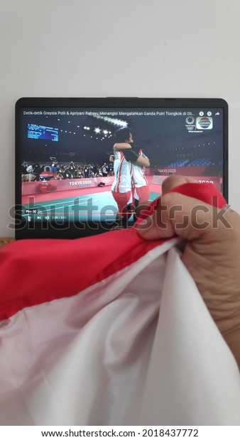 not focused. Watch on the laptop the moment Greysia\
Polii and Apriyani Rahayu from Indonesia won the gold medal for the\
women\'s doubles at the 2020 Tokyo Olympics. front view of the red\
and white flag