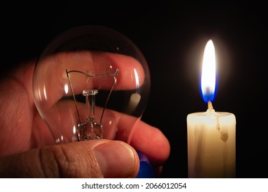 Not glowing light bulb illuminated by the light of a burning candle in complete darkness. Blackout, electricity off, energy crisis or power outage, concept image. 