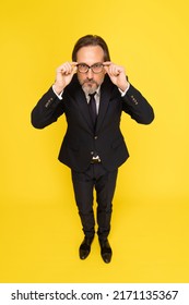 Not Happy, Serious Middle Aged Business Man Touching, Fixing His Eye Glasses Looking At Camera Isolated On Yellow Background. Handsome Mature Businessman In Black Suit. Business Concept. Copy Space.