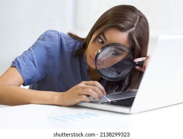 Not missing a speck of dirt.... Young woman using a magnifying glass while cleaning her laptop keyboard.
