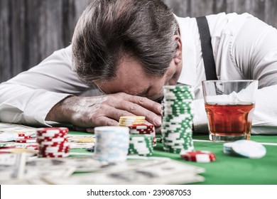 It is not my day. Depressed senior man in shirt and suspenders leaning his head at the poker table with money and gambling chips laying all around him - Shutterstock ID 239087053