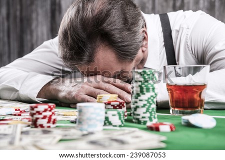 It is not my day. Depressed senior man in shirt and suspenders leaning his head at the poker table with money and gambling chips laying all around him