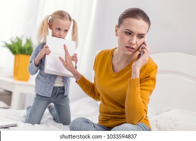 Not now.Pretty charming displeased mom communicating on phone while frowning and turning away from daughter