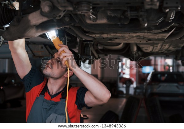 Not only strong hands needed but also some good\
sight. Man at the workshop in uniform fixes broken parts of the\
modern car.