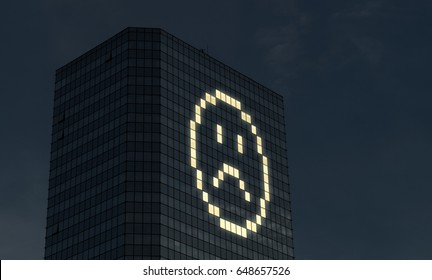 Not Satisfied And Unhappy Working Overtime. Late At Work And Doing Extra Hours. Bad Mood From Too Much Things To Do At Job. Icon And Sad Smiley Face Made By Office Building Window Lights At Night.