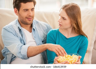 I Am Not Sharing Food! Beautiful Young Couple Sitting On The Couch Together And Watching TV