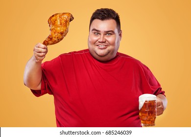 Not sporty fat man at oktoberfest, drinking beer and eating chicken leg on yellow background.