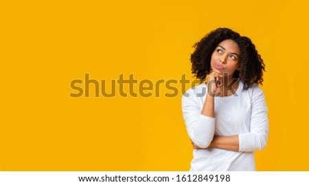 I'm not sure. Doubtful black woman thinking about something, touching her chin and looking away on yellow background, panorama with free space