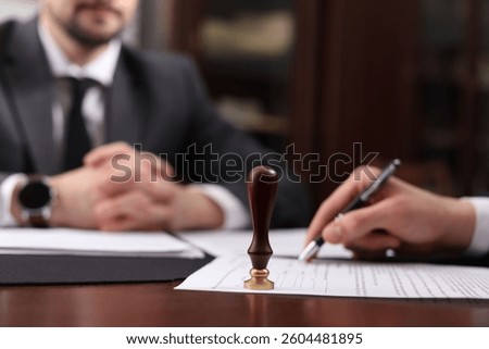 Notary and client signing document at table in office, selective focus
