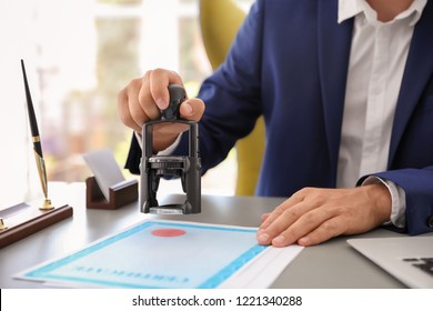 Notary stamping document at desk in office, closeup