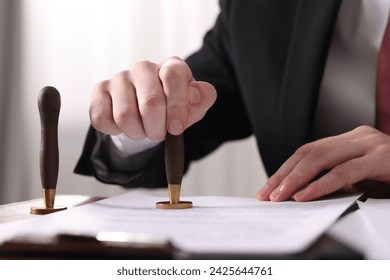 Notary stamping document at table in office, closeup
