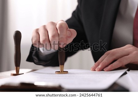 Notary stamping document at table in office, closeup