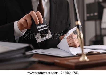 Notary stamping document at table in office, closeup