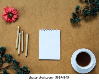 Note book, some wooden pencils and cup of coffee in the corner surrounded by dry red flower and branches of birch. Top view. Flat lay.