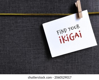Note clip with cloth pin on grey background with text written FIND YOUR IKIGAI, Japanese concept of a reason for living life, to find what feeds motivation to get out of bed each morning
