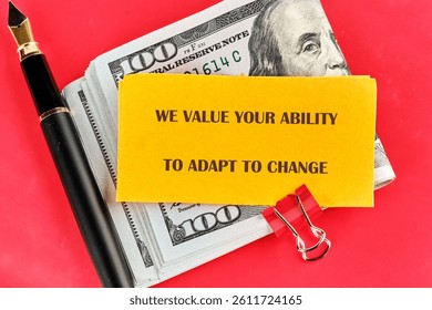 A note emphasizing the importance of adaptability is clipped next to a stack of cash and an elegant pen, creating a striking visual against the bright red backdrop.