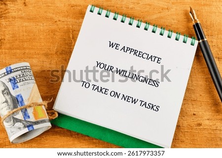 A note expressing appreciation for taking on new tasks is placed on a wooden table alongside rolled currency and a pen, creating a motivational atmosphere for work.