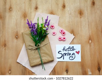 A note with hello Spring text and a gift box with flowers on rustic wooden table 