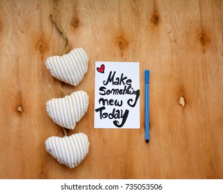 A note with make something new today and a pen on wooden table with white hearts