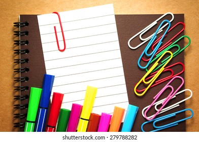 Note paper clip on notebook with colorful marker pens and paperclips on brown cardboard background