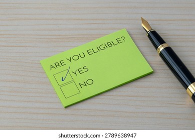 A note with the question Are you eligible? and a checked Yes box on a wooden desk. Qualification, approval, applications, and specific criteria concept.