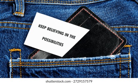 A note reminding to keep believing is placed with a black wallet inside the back pocket of blue denim jeans. The stitching adds a touch of craft.