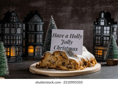 Note with saying HAVE A HOLLY JOLLY CHRISTMAS. Traditional German Christmas stollen cake in background of handmade festive decor. Winter holiday treats. Vegan baking recipe - Powered by Shutterstock